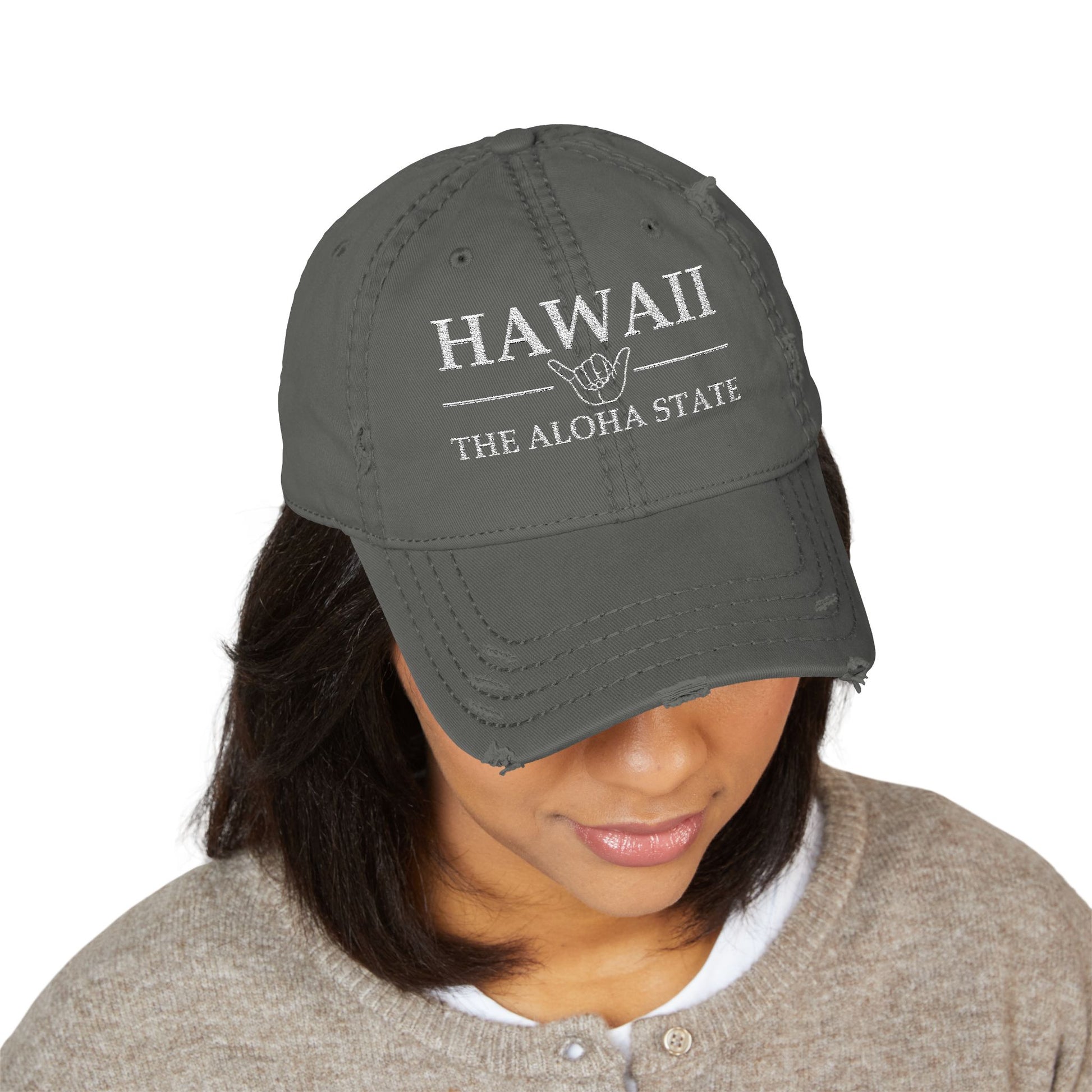 Person wearing a gray cap with 'HAWAII THE ALOHA STATE' text and hand symbol  embroidered in white thread