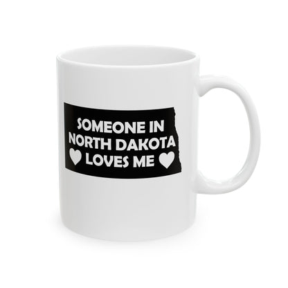 White mug with a black label reading 'Someone in North Dakota loves me' on a white background